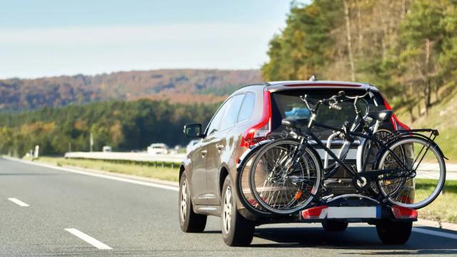 Car with a rear bike carrier driving on a road, illustrating the fuel cost of carrying extra gear.